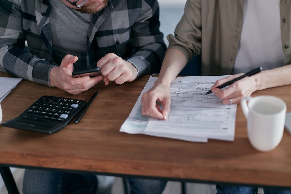 A couple at a kitchen table working through paperwork with a calculator