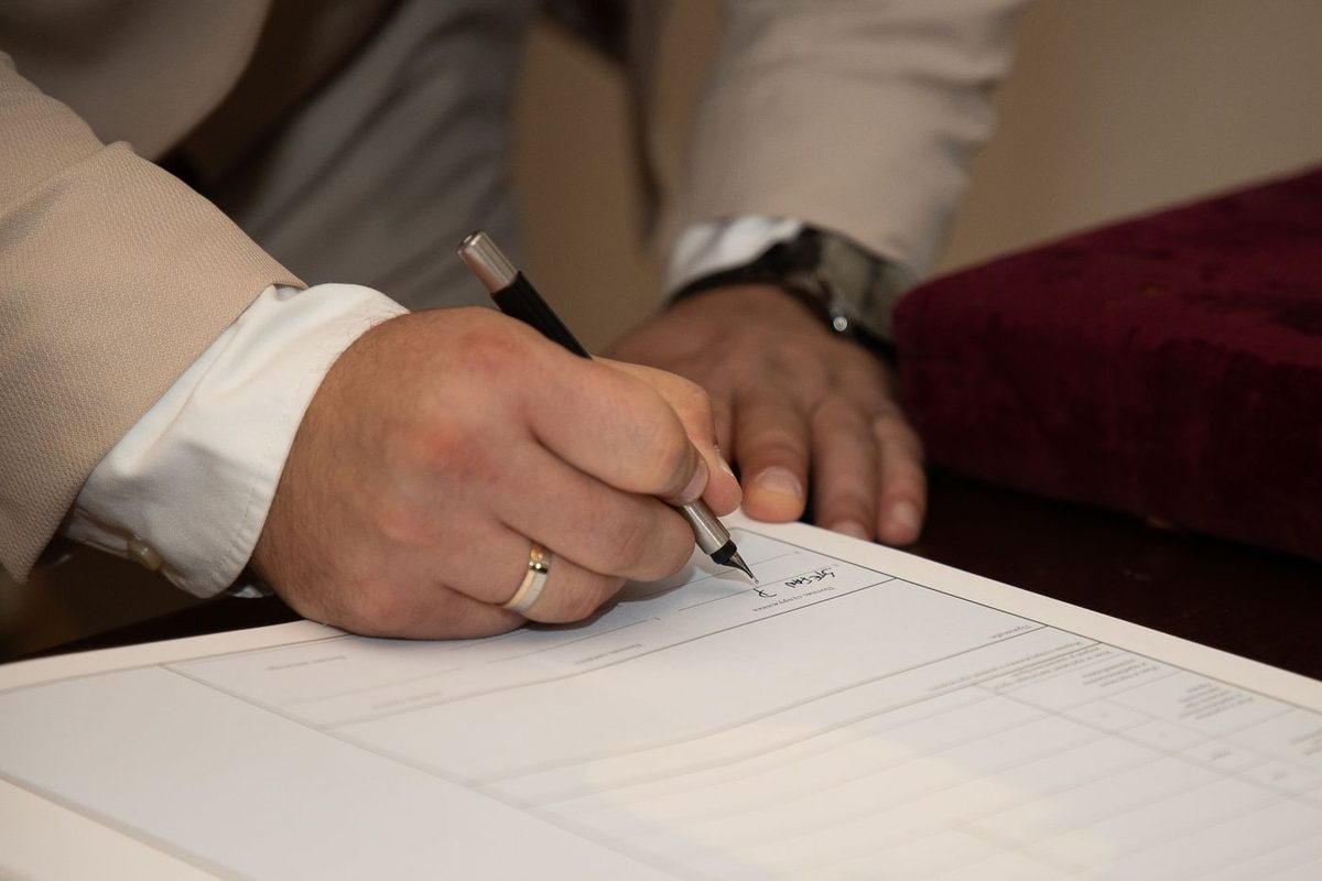 A hand wearing a wedding ring signing a printed form